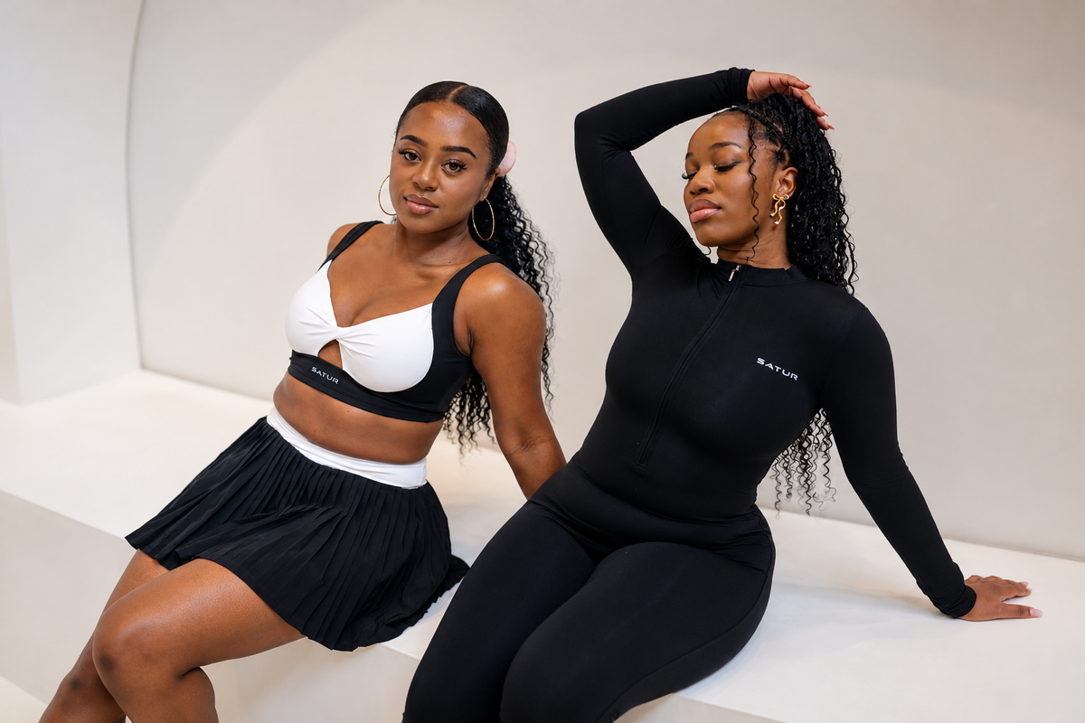 Two women wearing the SaturSculpt Monochrome Pleated Tennis Set and black zip-up jumpsuit