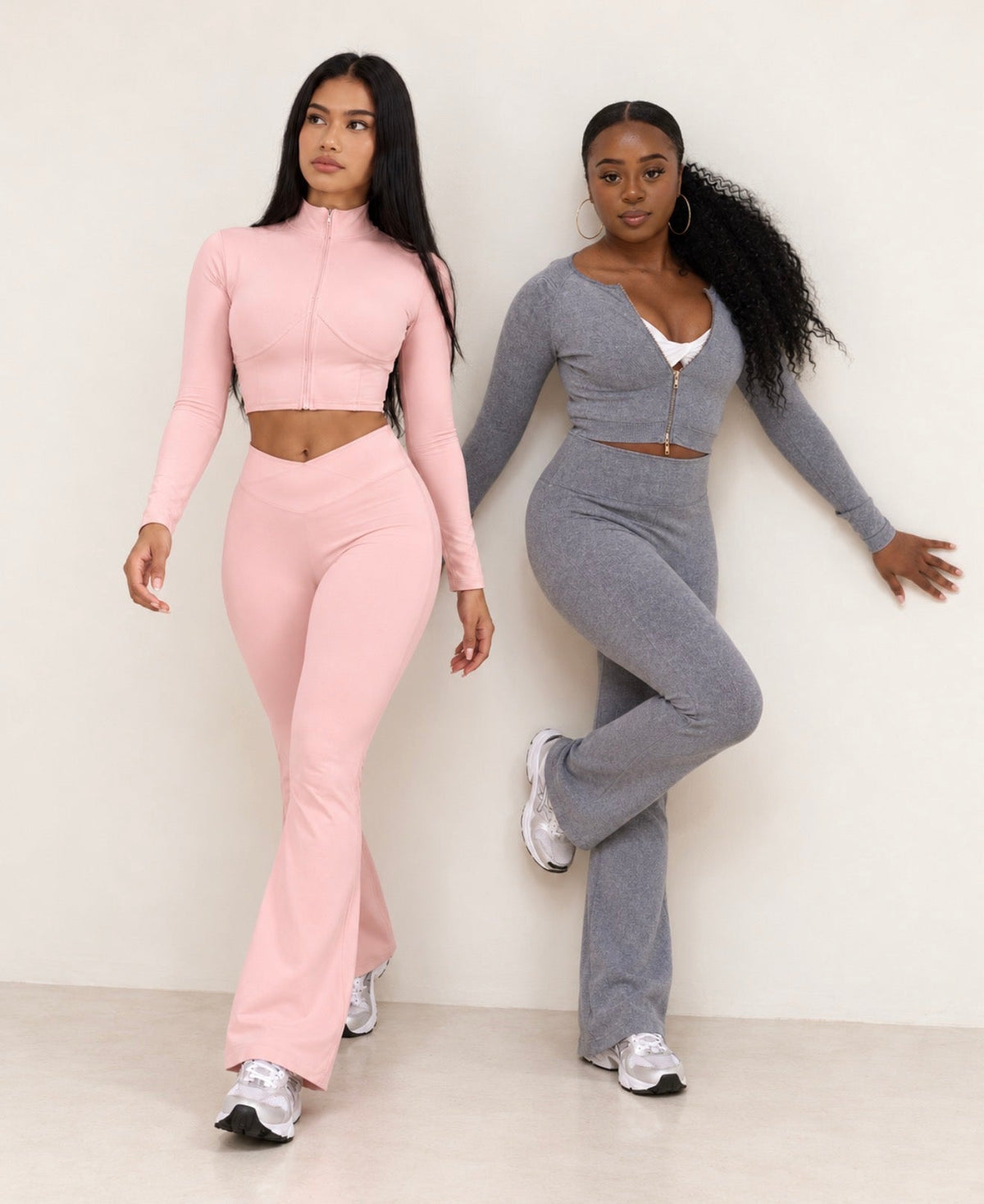 Two women wearing SaturSculpt zip-up flare sets in blush pink and grey